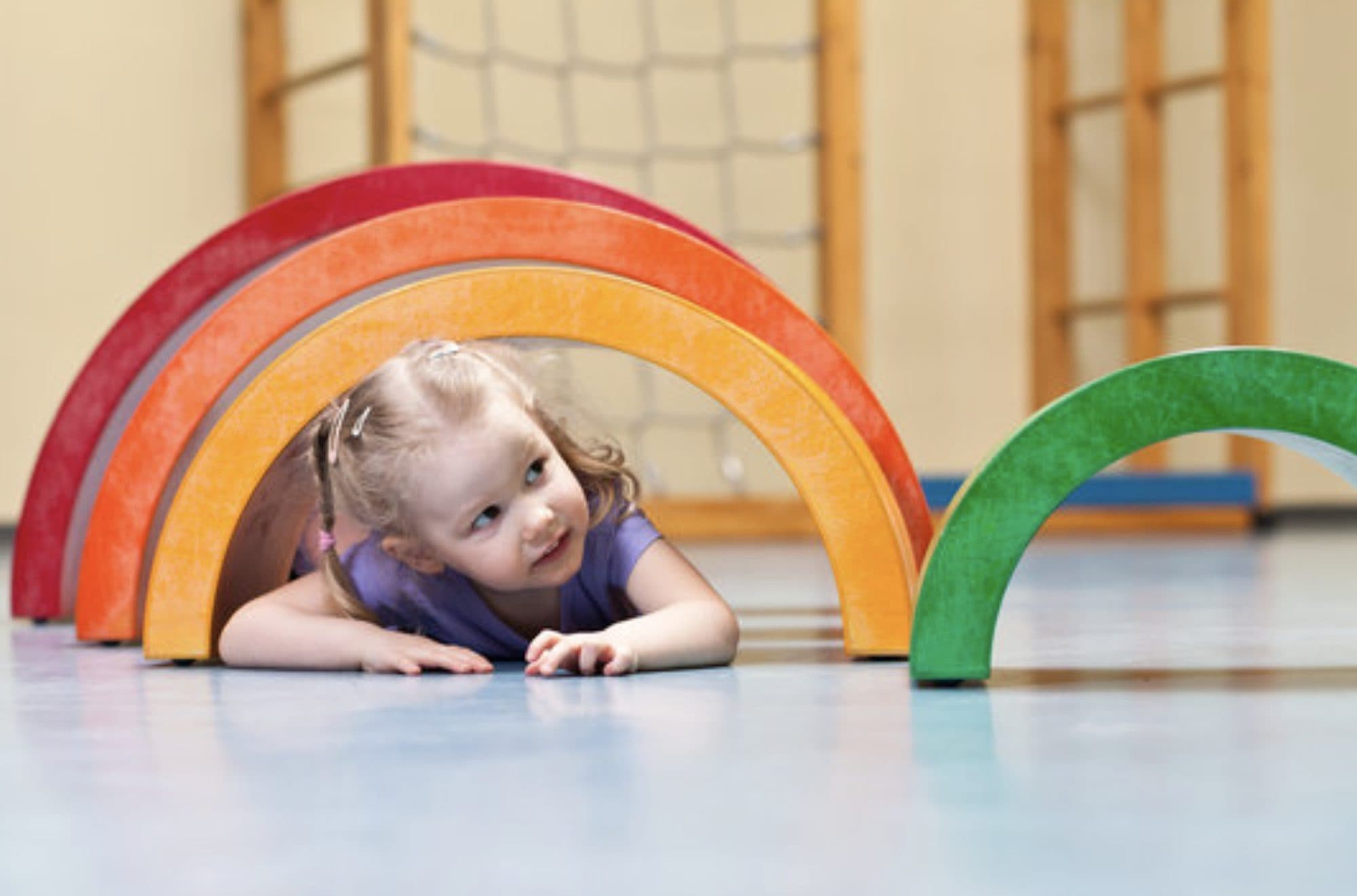Mädchen krabbelt durch einen Tunnel aus bunten Regenbogenbögen