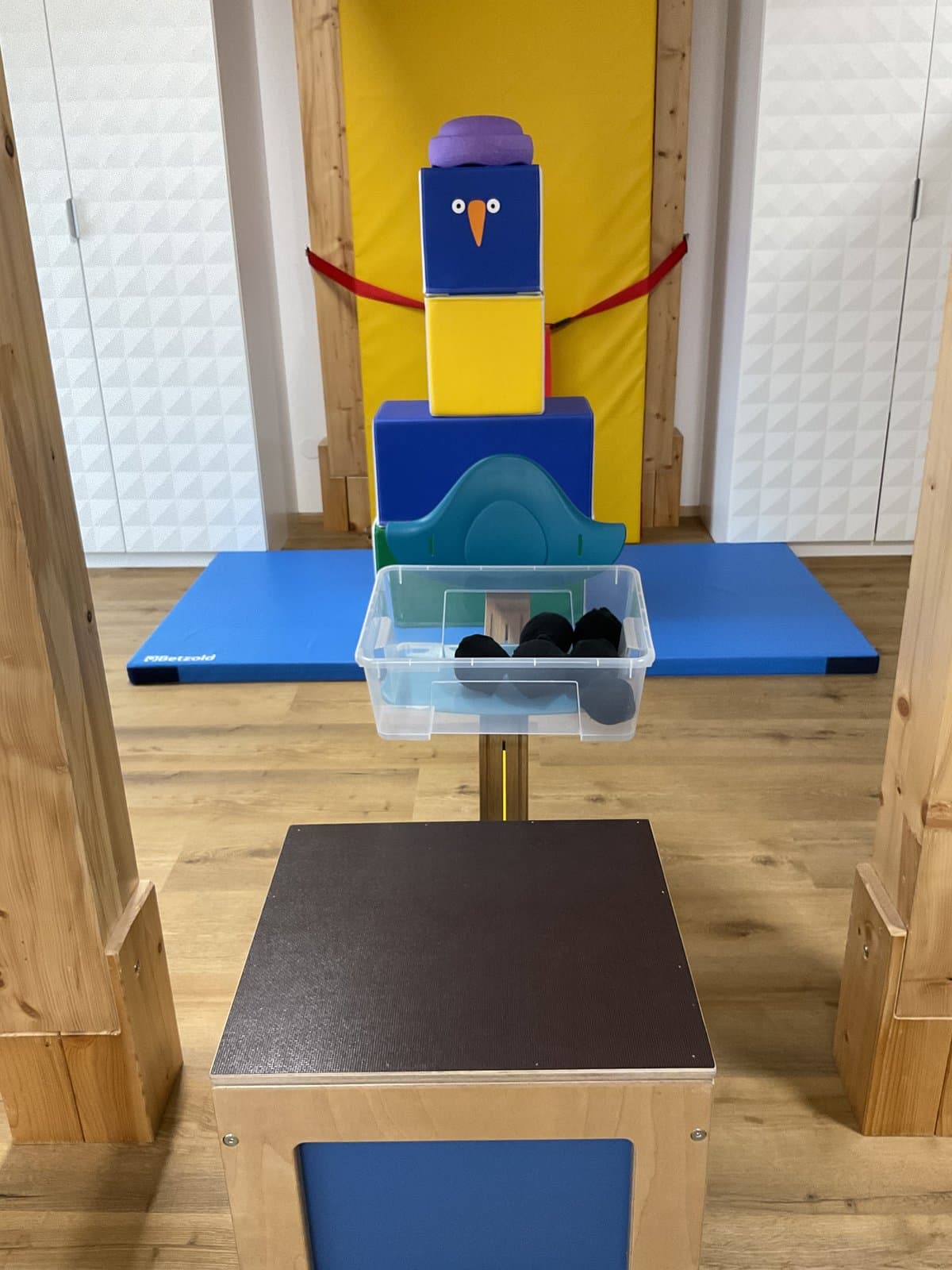 Figur aus bunten Softbausteinen auf einer blauen Turnmatte, davor eine Kiste und ein Hocker