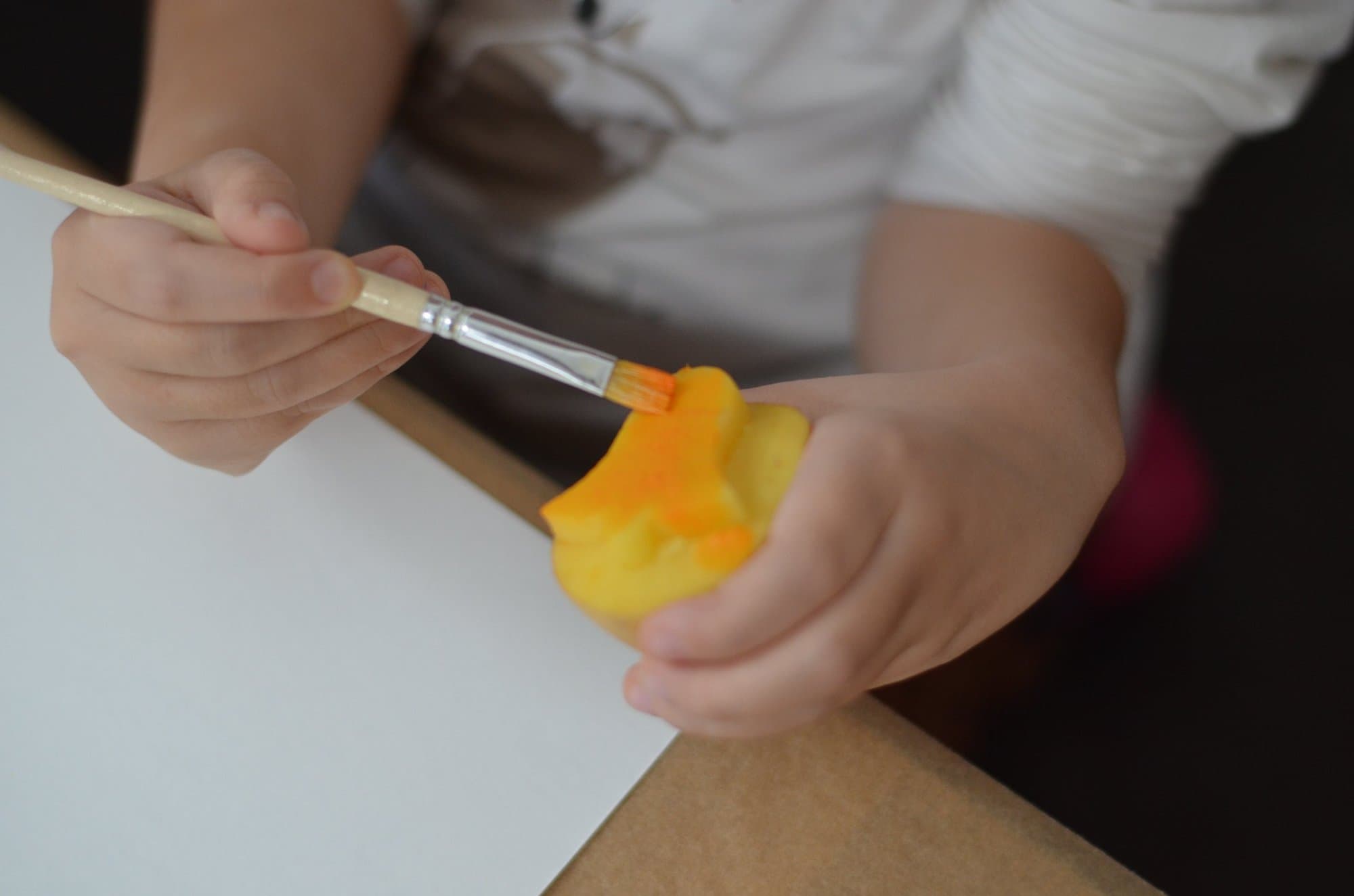 Kinderhand bemalt einen Kartoffelstempel mit einem Pinsel in Orange