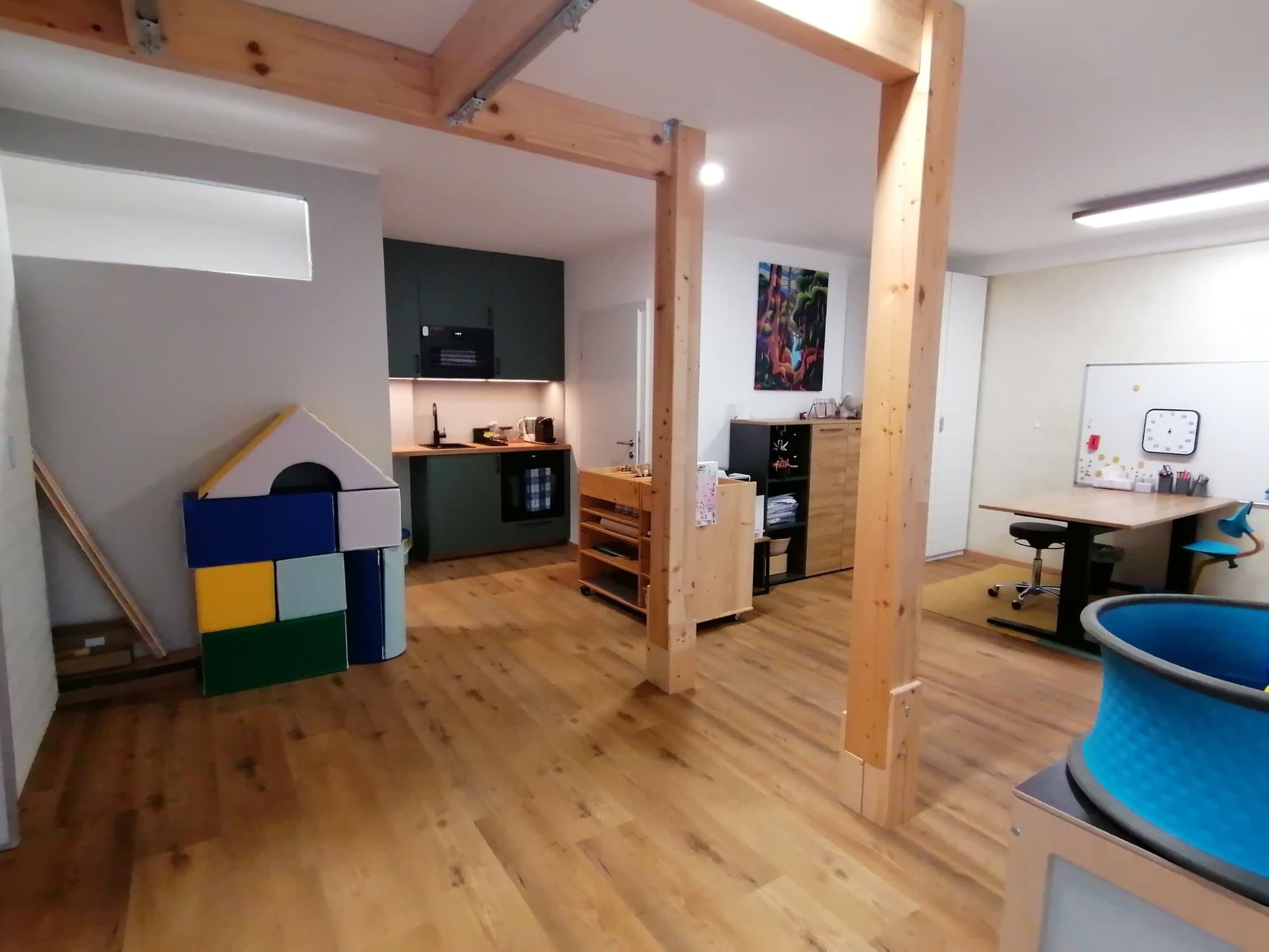 Praxisraum mit einem Haus aus Softbausteinen, kleiner Küche, Regalen und Arbeitstisch